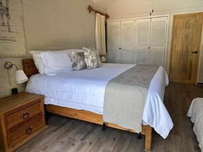 A bedroom with a wooden bed, a nightstand, a lamp, a wardrobe, and a wall with a sketch.