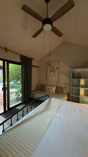 A bedroom with a bed, a ceiling fan, a window with a view, and a bookshelf.