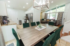 Eine moderne Küche mit weißen Schränken, einem Edelstahlkühlschrank und einem Essbereich mit einem Holztisch und grünen Sitzmöbeln.