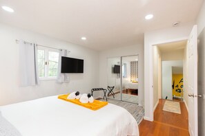 Ein Hotelzimmer mit Bett, Flachbildfernseher, Fenster mit Vorhängen, Spiegel und Tür zu einem anderen Raum.