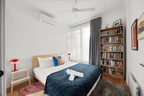 A bedroom with a bed, a bedside table, a bookshelf, and a ceiling fan. - 3BR Townhouse with Private Terrace & Double Garage (Northcote)