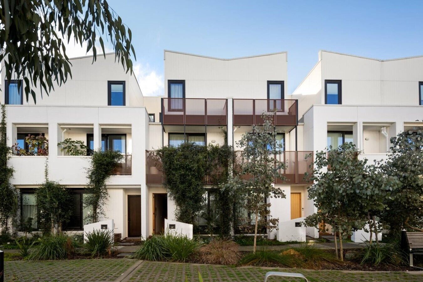 A modern multi-story residential building with balconies, a central courtyard, and surrounding greenery.