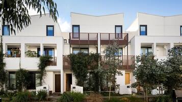 A modern multi-story residential building with balconies, a central courtyard, and surrounding greenery.