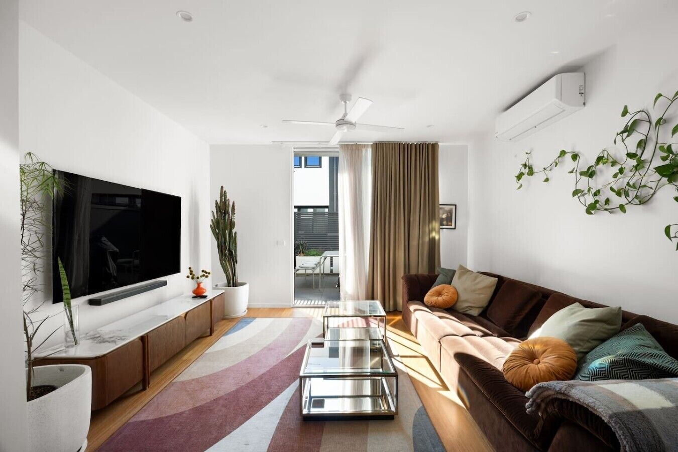 A modern living room with a flat-screen TV, a ceiling fan, a sofa, a coffee table, and a potted plant.