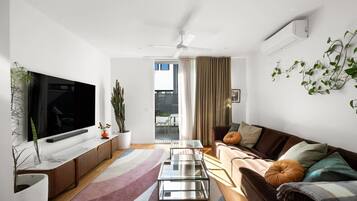 A modern living room with a flat-screen TV, a ceiling fan, a sofa, a coffee table, and a potted plant.