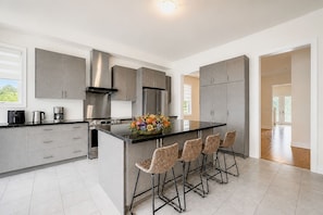 A modern kitchen with grey cabinets, a central island with bar stools, and a coffee maker on the counter.