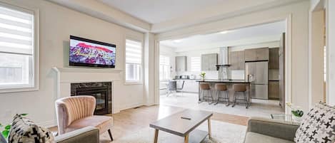 A spacious living room with a fireplace, a television, and a kitchen in the background.