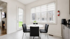 A modern dining area with a round table, four chairs, and a view of a brick building through large windows.
