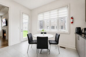 A modern dining area with a round table, four chairs, and a view of a brick building through large windows.
