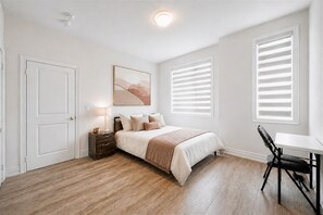 A bedroom with a bed, bedside table, lamp, and a chair.