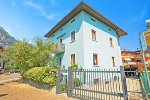 Ein hellblaues Gebäude mit geschlossenem Eingangsbereich, einem Balkon und einem Berg im Hintergrund.