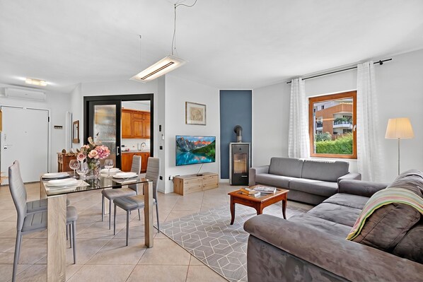Ein modernes Wohnzimmer mit einer Couch, einem Esstisch und einer durch eine offene Tür einsehbaren Küchenzeile.