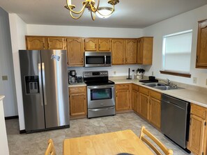 A kitchen with wooden cabinets, stainless steel appliances, a coffee maker, and a dishwasher. - Cozy 3-bedroom bungalow in Fort Wayne (Fort Wayne)
