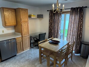 A kitchen with wooden cabinets, a dining table with chairs, a chandelier, and a view through curtains. - Cozy 3-bedroom bungalow in Fort Wayne (Fort Wayne)