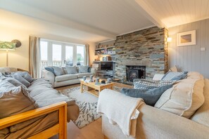 A cozy living room with a stone fireplace, a sofa set, a television, and a bookshelf. - Little Palm Trees is walking distance of the charming surf-village of Polzeath (Polzeath)