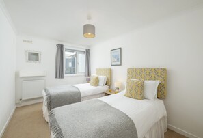 Ein Hotelzimmer mit zwei Einzelbetten, einem fenster mit Vorhängen, einem Heizkörper, einem Nachttisch mit Lampe und einem gerahmten Bild an der Wand.