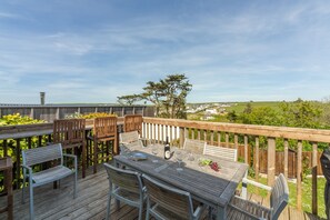 A wooden deck with a table set for dining, surrounded by chairs, overlooking a scenic landscape. - Little Palm Trees is walking distance of the charming surf-village of Polzeath (Polzeath)