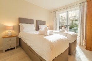 Ein Doppelbett mit weißer Bettwäsche, ein Nachttisch mit Lampe und Blick durch eine Glastür hinaus.