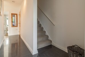 Ein heller, moderner Flur mit poliertem Boden, einem spiegeln deutenden Holzbalken und einer Treppe mit grauem Teppich.