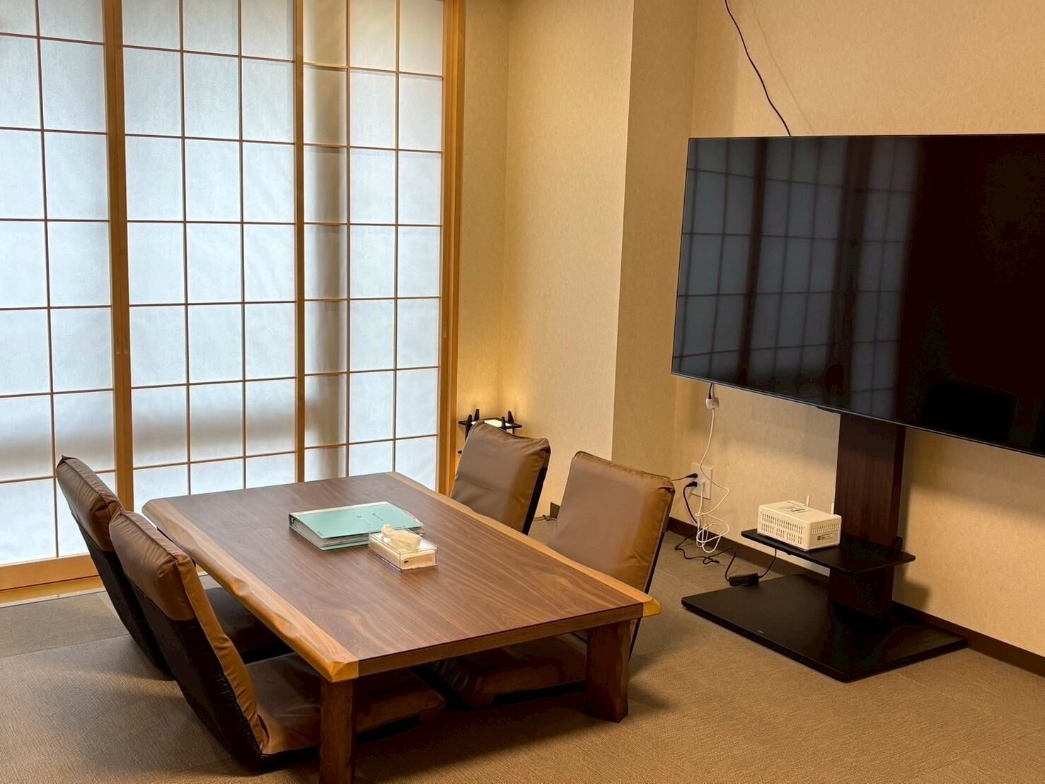 A conference room with a wooden table, chairs, a large flat-screen TV, and a traditional Japanese shoji screen.