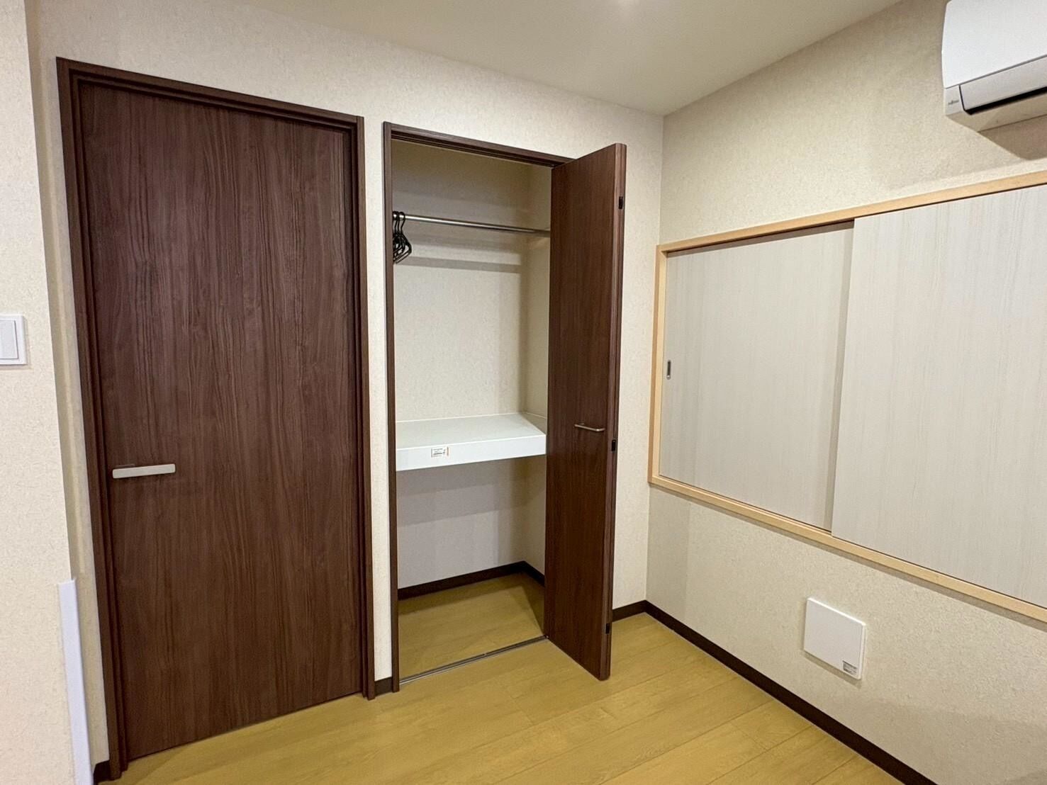 A room with a wooden wardrobe, a white shelf, and a white wardrobe with a wooden frame.