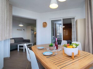 A dining area with a wooden table, white chairs, a bowl of fruit, and a bottle of wine. - Hernando I by Interhome (Calpe/Calp)