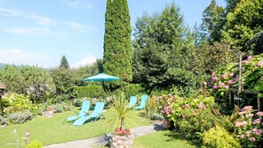 Un jardín con un camino, una sombrilla azul y dos sillones de relax.