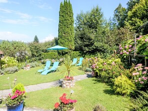 Ein Garten mit einem Weg, einem blauen Sonnenschirm und zwei Liegestühlen.