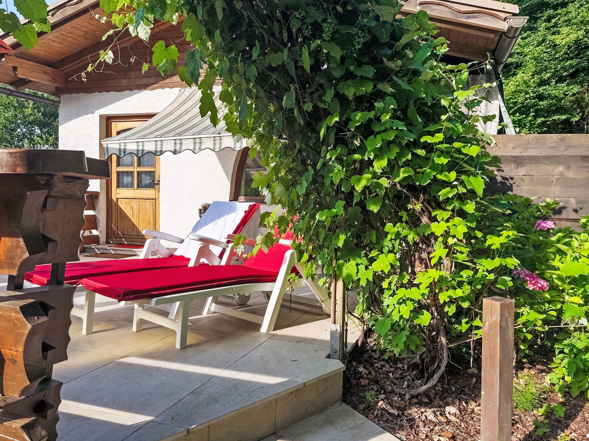 Ein überdachter Außenbereich mit zwei Loungestühlen, einer Holzw pergola und einem weißen Gebäude mit Holztür.