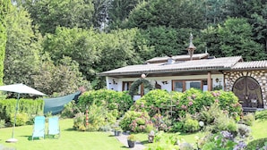 Una casa con jardín, una terraza de madera y un árbol grande al fondo.