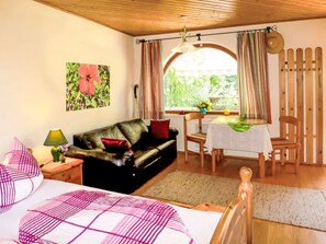 Ein gemütliches Zimmer mit einer Couch, einem Esstisch mit Stühlen, einem Bett und einem Fenster mit Vorhängen.