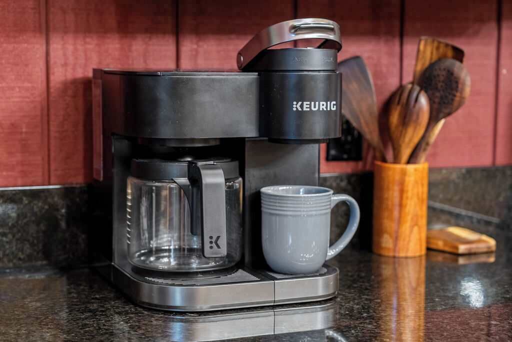 A Keurig coffee maker with a mug and a wooden spoon holder on a kitchen counter.