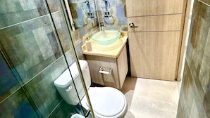 A bathroom with a glass shower enclosure, a toilet, a sink with a glass basin, and a wooden cabinet. - Business & Leisure Premium Apartment | Fast Wi-Fi & Prime Location (Villavicencio)