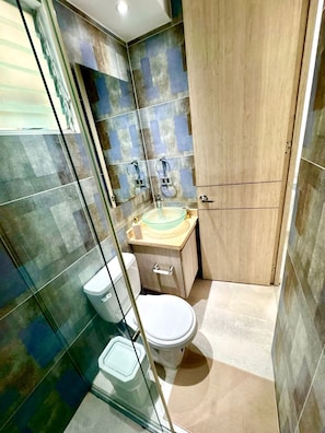 Une salle de bain avec une douche à parois de verre, des toilettes, un lavabo avec un récipient en verre et un meuble en bois.