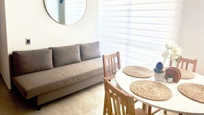 A room with a sofa, a round table with placemats, a mirror, and a window with blinds. - Business & Leisure Premium Apartment | Fast Wi-Fi & Prime Location (Villavicencio)