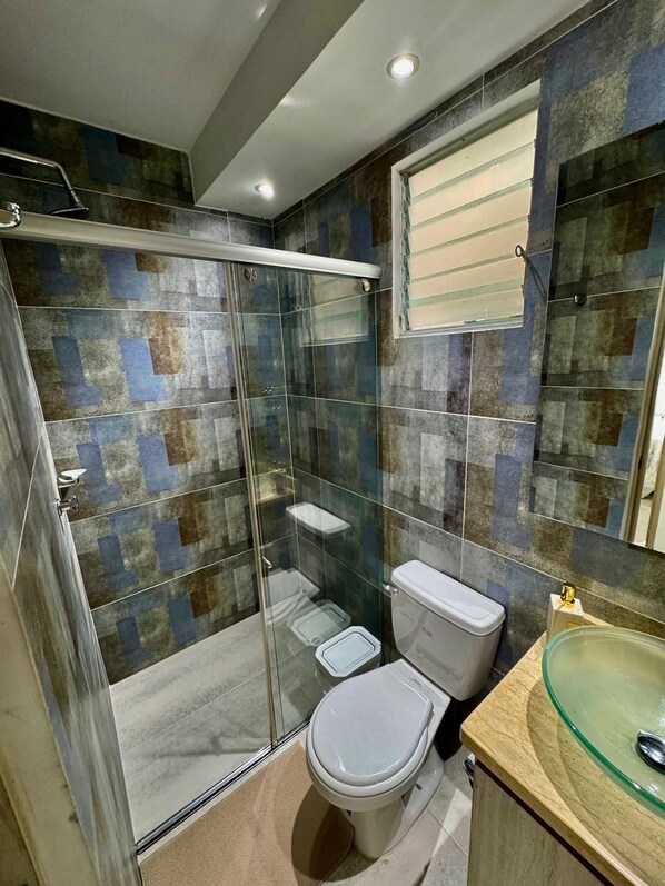 A modern bathroom with a glass-enclosed shower, a toilet, and a glass sink.