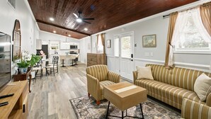 A spacious living area with a wooden ceiling, a striped sofa, a coffee table, and a dining area with chairs and a table.