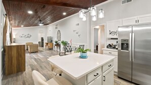 A modern kitchen with a stainless steel refrigerator, white cabinetry, a central island with a potted plant, and a wooden ceiling.