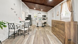 A modern kitchen with white cabinets, a wooden ceiling, and a dining area with a table and chairs.