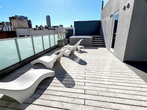 Eine Dachterrasse mit Liegestühlen, einer Glasreling und Blick auf Gebäude im Hintergrund.