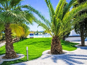 A landscaped area with palm trees, a pool, and a view of a body of water. - Casa do Lago by Interhome (Estoi)
