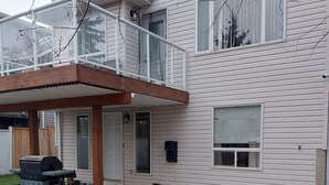 A two-story house with a covered patio, a grill, and a hose on the lawn. - Gateway to Banff | Cozy 2BR Sleeps 6 | NW Calgary (Calgary)