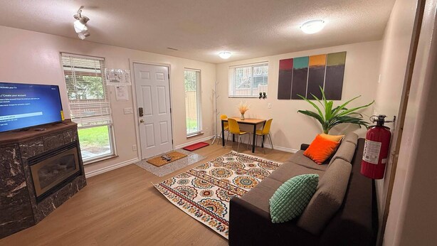 A living room with a fireplace, a television, a sofa, a coffee table, and a dining area with chairs. - Gateway to Banff | Cozy 2BR Sleeps 6 | NW Calgary (Calgary)