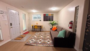 A living room with a sofa, a patterned rug, a dining area with a table and chairs, and a fire extinguisher on the wall. - Gateway to Banff | Cozy 2BR Sleeps 6 | NW Calgary (Calgary)