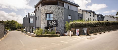A modern building with a stone facade, a sign for 'The Harlyn Tap Room & Kitchen,' and a small outdoor seating area.
