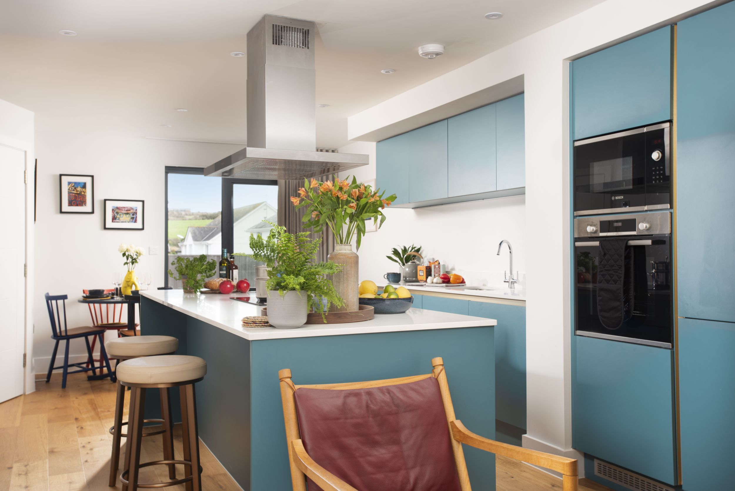 Een moderne keuken met een centraal eiland, blauwe kastjes en een Bosch oven.