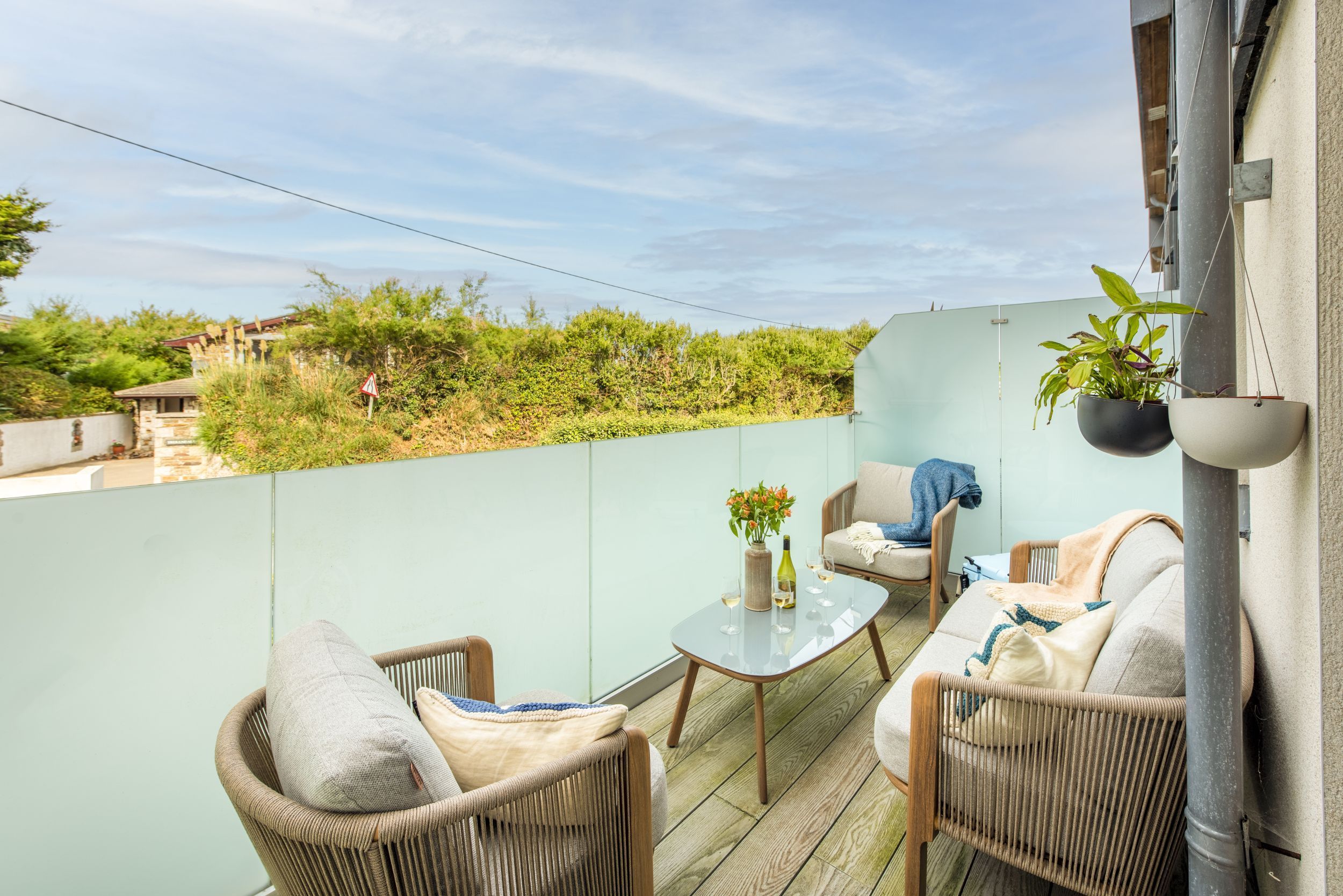 Un balcon agrémenté de meubles en osier, d’une table en verre et de plantes en pot.