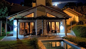Et moderne hus med swimmingpool, udendørs møbler og en overdækket terrasse.