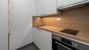 Une cuisine moderne avec des meubles blancs, un plan de travail en bois, un évier en acier inoxydable et un four.