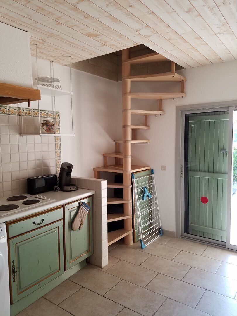 A kitchen with a wooden staircase, a coffee maker, and a green door.